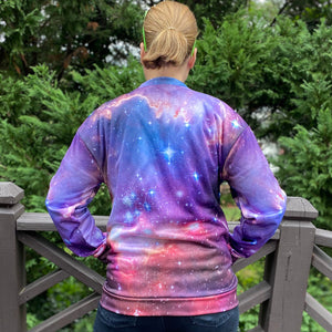 Emily wearing the NGC 602 light jacket, shown from the back with her hands in the front pockets, with a fence and greenery in the background