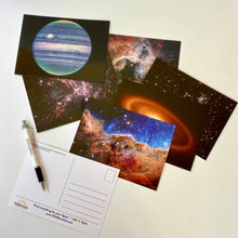 Load image into Gallery viewer, JWST First Year postcards arranged on a white surface, with one showing the back, and a STARtorialist pen