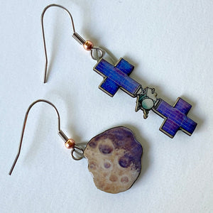 Mismatched earrngs made from upcycled paperboard, one an illustration of the Psyche mission soacecraft and the other the asteroid Psyche with two distinctive craters in partial shadow, shown resting on a white background.