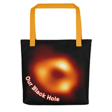 Load image into Gallery viewer, Digital mock up of a black tote bag with yellow handle printed with the Event Horizon Telescope image of the Sgr A* supermassive black hole in the Milky Way Galaxy with curved text reading "Our Black Hole" in red and white on one side.