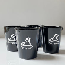 Load image into Gallery viewer, Four black shot glasses with white Artemis logo arranged in a group with one at the front
