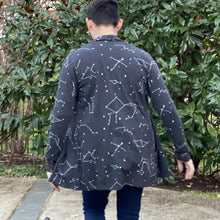 Load image into Gallery viewer, Seen from behind, Matthew wears a dark gray cardigan with white constellation stars and lines, mid-stride with arms away from his sides and the cardigan flaring out a bit, with green foliage in the background.