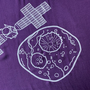 illustration detail of the Psyche asteroid and part of the spacecraft in silver ink on a purple plush-weave scarf