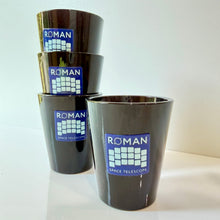 Load image into Gallery viewer, Four glossy black ceramic shot glasses stacked and standing in front, each printed with a blue and white 'ROMAN SPACE TELESCOPE' logo, on a white surface against a white wall.