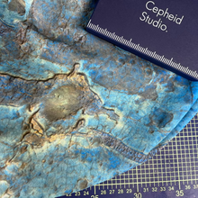 Load image into Gallery viewer, A close-up of a blue and brown marbled fabric printed with a HiRISE image of the Martian surface, placed over a dark blue-purple  measuring grid with a Cepheid Studio box on top