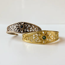 Load image into Gallery viewer, Two cuff bracelets with black opal center stones, surrounding solar corona-like design, and crescents scattered around the band, stacked offset (silver tone on top of gold tone) on a white background.