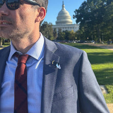 Load image into Gallery viewer, A man in a suit and tie with a Roman spacecraft acrylic pin in the button hole of his lapel stands outside in a sunny day with the dome of the US Capitol Building in the distance, wearing sunglasses and looking away from the camera