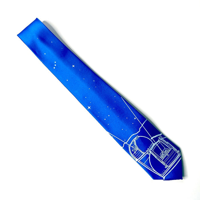 Keck Observatory Necktie, bright blue tie with observatory domes and night sky illustration in white, folded in half laid flat diagonally on a white background