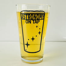 Load image into Gallery viewer, Astronomy on Tao logo pint glass filled with light yellow beer on a white nackground