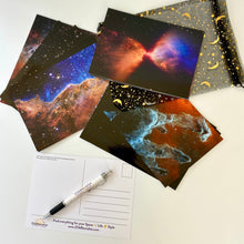 Load image into Gallery viewer, JWST First Year postcards arranged on a white surface, with one showing the back, and a STARtorialist pen and a black and gold organza bag