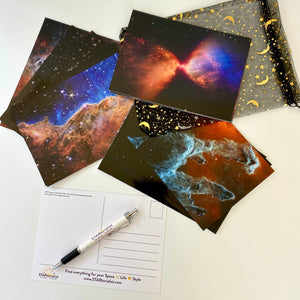 JWST First Year postcards arranged on a white surface, with one showing the back, and a STARtorialist pen and a black and gold organza bag
