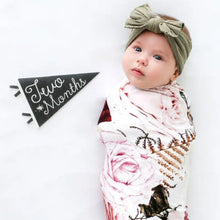 Load image into Gallery viewer, Baby wrapped in a floral blanket with a green headband, standing next to a 'Two Months' sign.