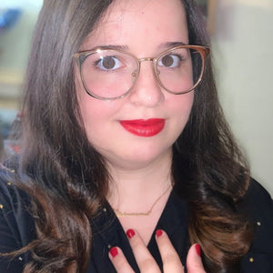 Katherine wearing the gold Astronomer nameplate necklace with a black gold-star-print shirt, red lipstick and nail polish