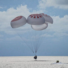 Load image into Gallery viewer, Dragon crew capsule spashdown with four deployed parachutes and an approaching boat.