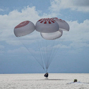 Dragon crew capsule spashdown with four deployed parachutes and an approaching boat.