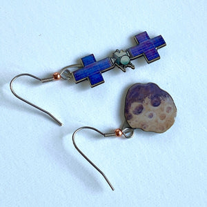 Mismatched earrngs made from upcycled paperboard, one an illustration of the Psyche mission soacecraft and the other the asteroid Psyche with two distinctive craters in partial shadow, shown resting on a white background.