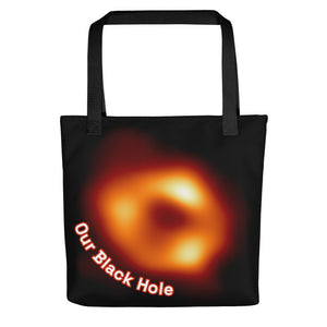 Digital mock up of a black tote bag with black handle printed with the Event Horizon Telescope image of the Sgr A* supermassive black hole in the Milky Way Galaxy with curved text reading "Our Black Hole" in red and white on one side.