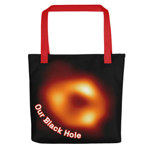 Digital mock up of a black tote bag with red handle printed with the Event Horizon Telescope image of the Sgr A* supermassive black hole in the Milky Way Galaxy with curved text reading "Our Black Hole" in red and white on one side.