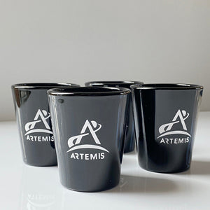 Four black shot glasses with white Artemis logo arranged in a group with one at the front