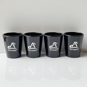 Four black shot glasses with white Artemis logo in a row